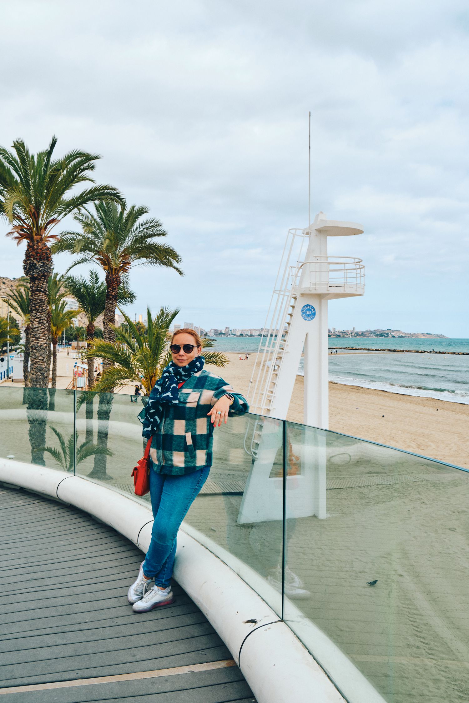 Scenic beachfront boardwalk with palm trees and lifeguard tower along the Mediterranean coast.