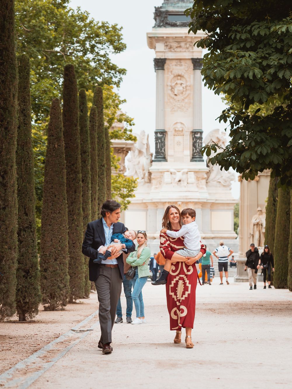 Elegant family strolling down tree-lined path in front of historic building.