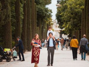 Family walking along tree-lined path in park with other visitors.