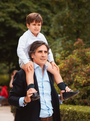 Child riding on shoulders through park pathway.