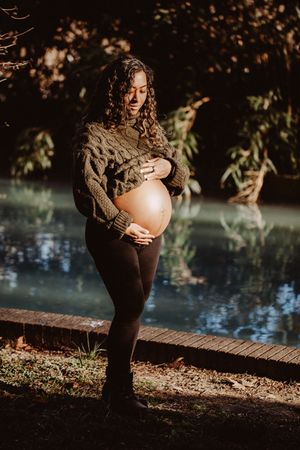 Maternity photo of woman in knit sweater by water at sunset.