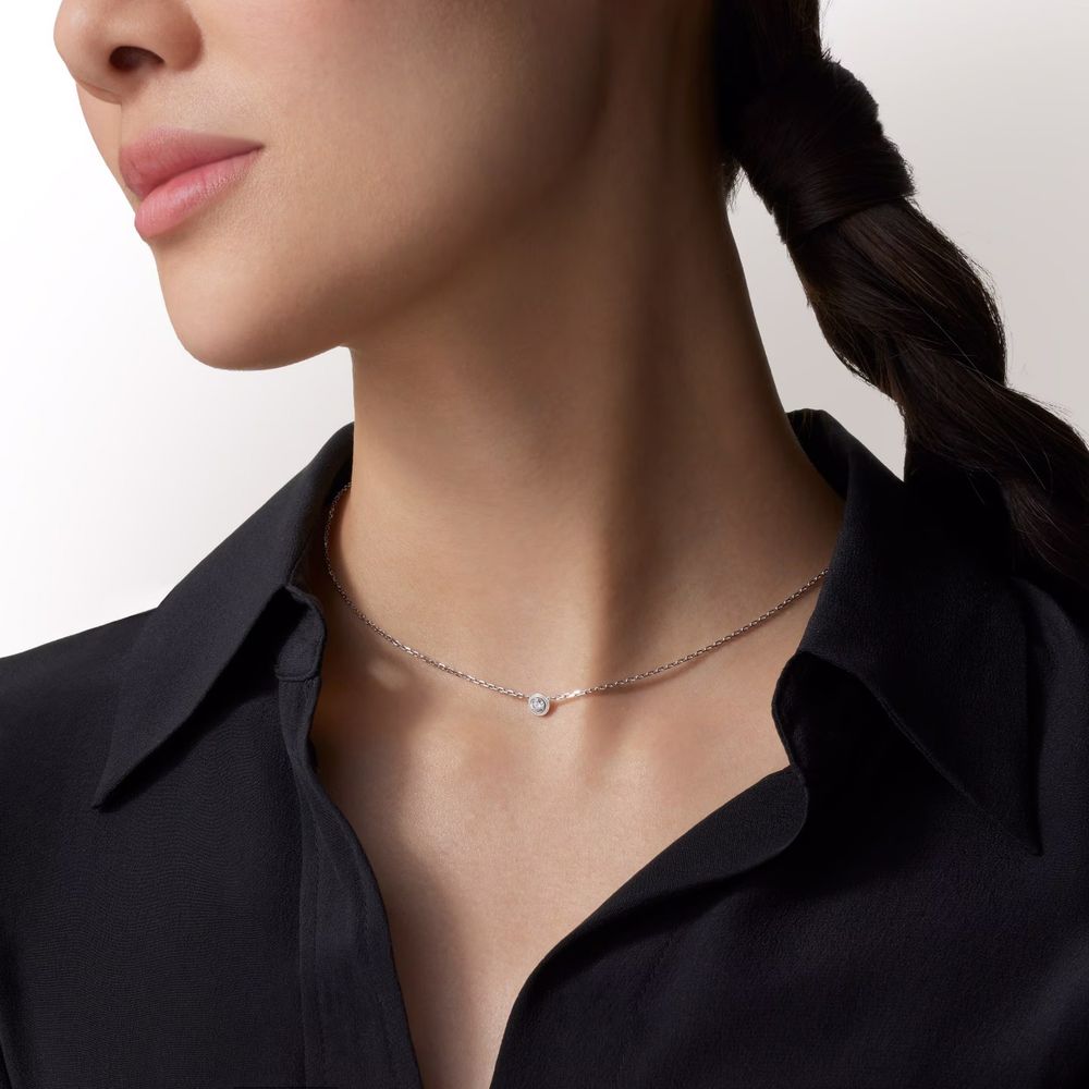Close-up view of a silver necklace with delicate chain and pendant against a dark background.