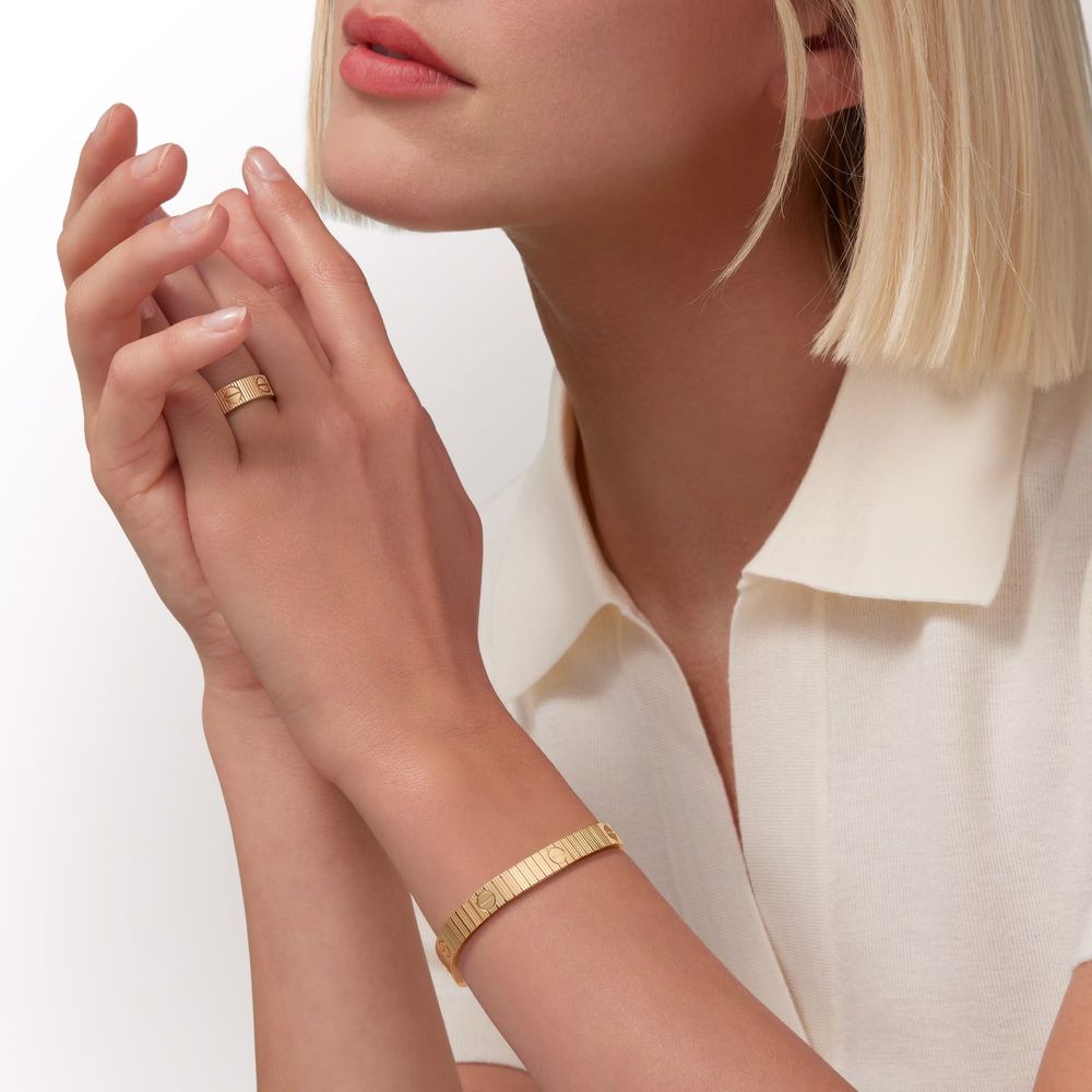 Elegant gold bangle bracelet and ring shown on model wearing white collared top against white background.