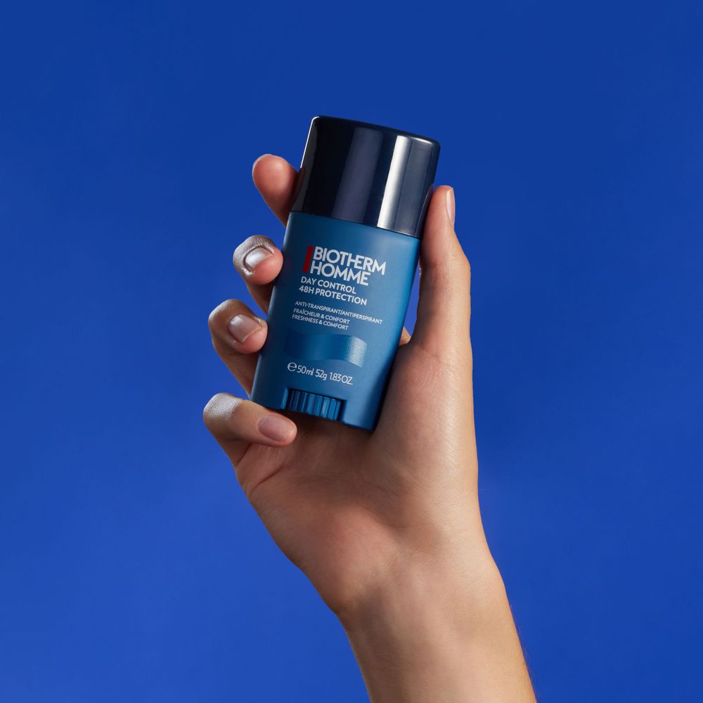Hand holding a blue Biotherm Homme deodorant stick against a bright blue background.