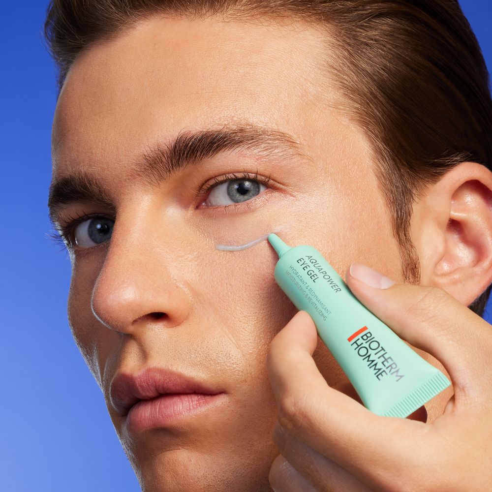 Mint green concealer product being applied under the eye area against a vibrant blue background.