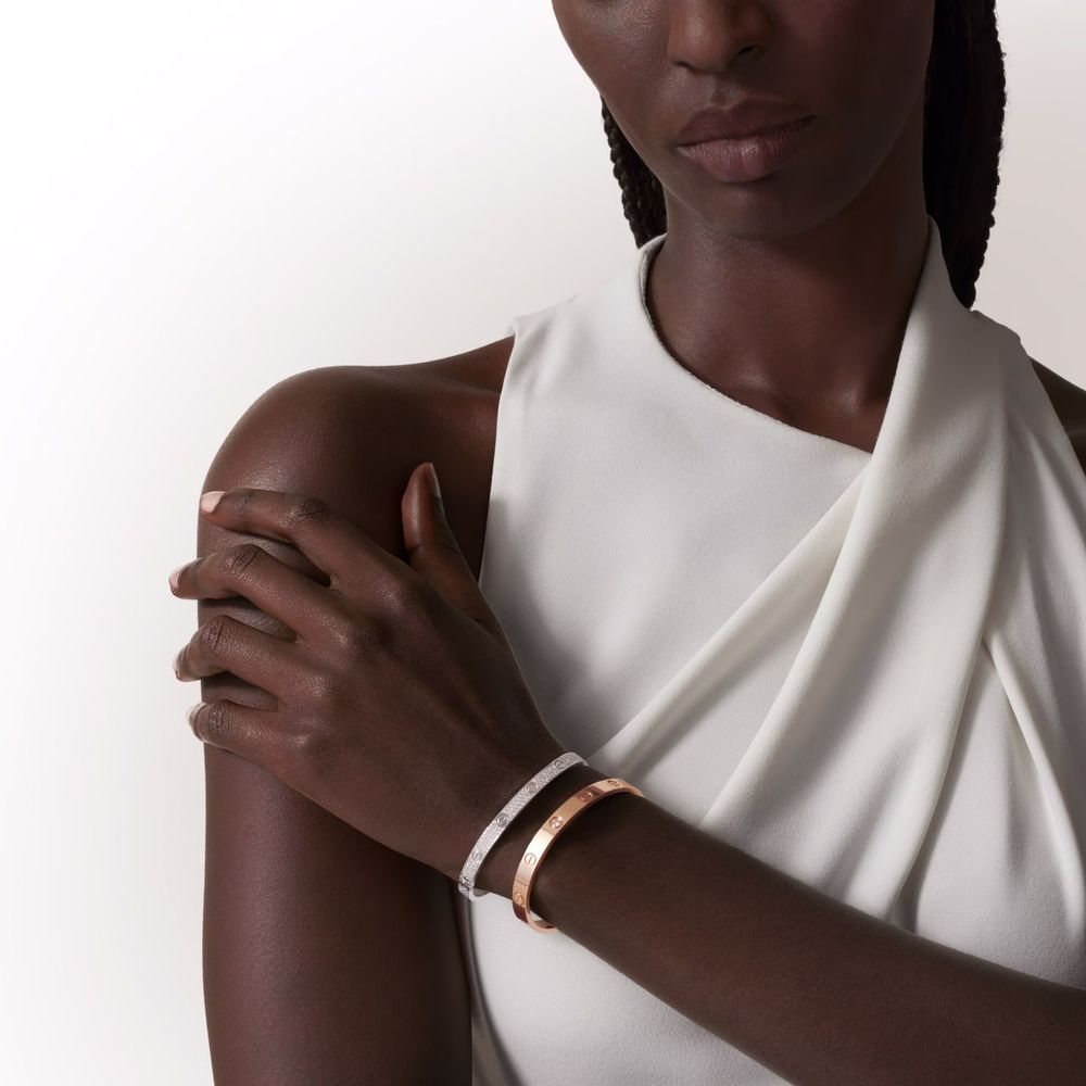 Close-up of a sleek white bracelet worn on dark skin against a white one-shoulder top.
