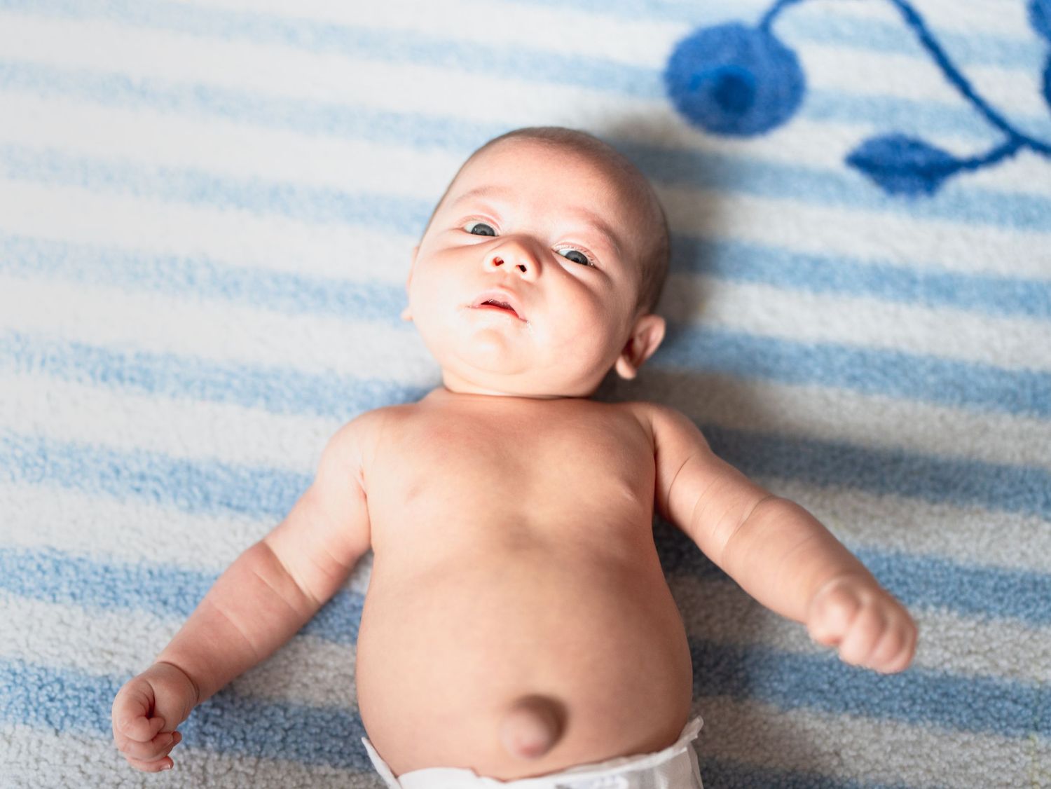Newborn baby laying on blue and white striped blanket.