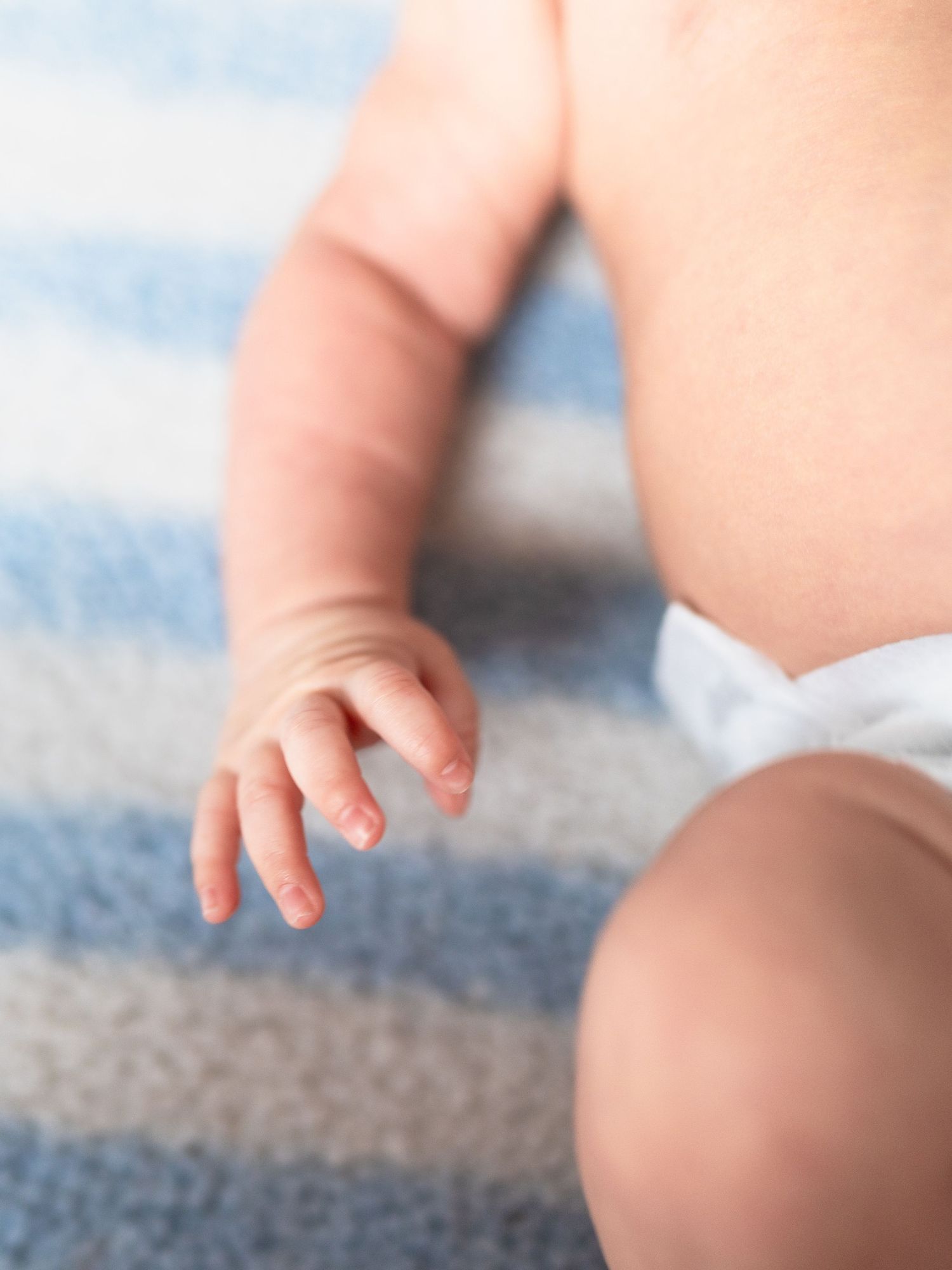 Close up of baby's tiny hands against blue and gray textured fabric.