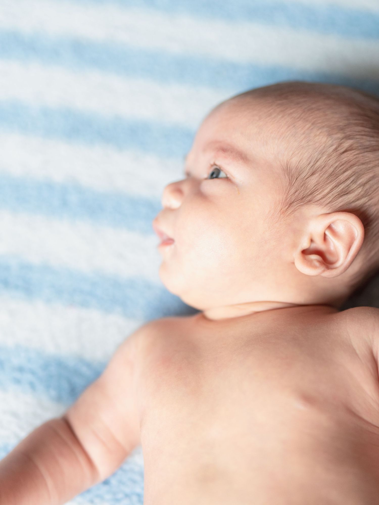 Profile view of sleeping newborn on blue striped blanket.