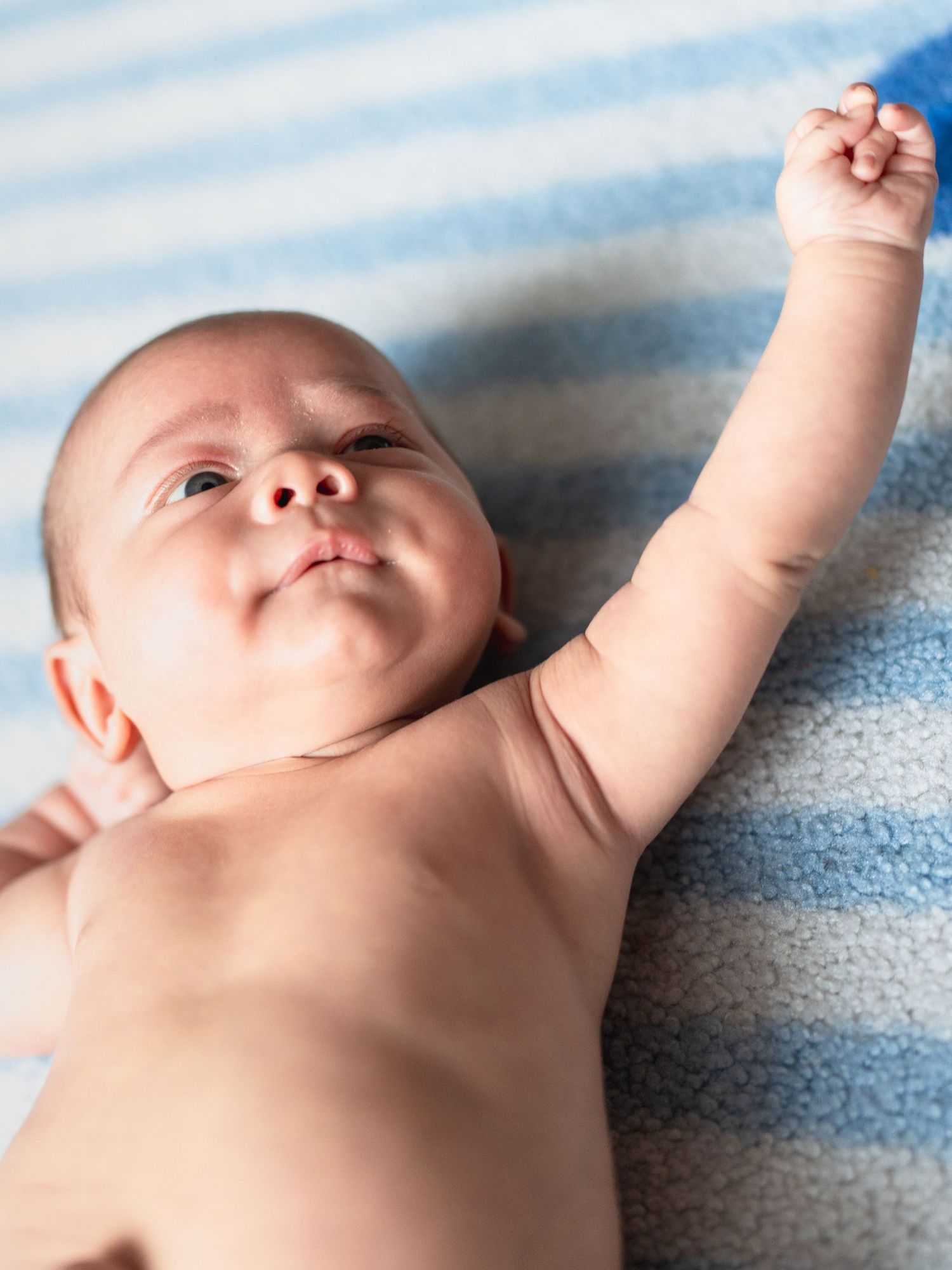 Baby stretching arms while lying on blue striped blanket in natural light.