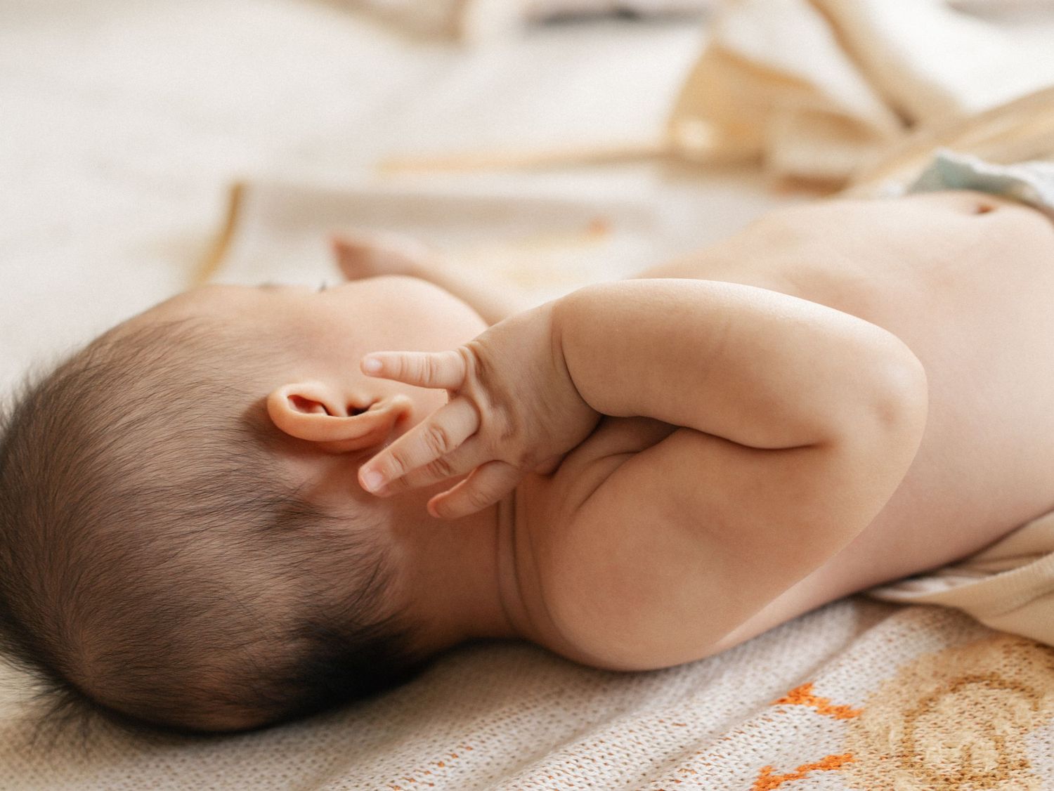 A sleeping baby lies on soft beige bedding in a peaceful pose.