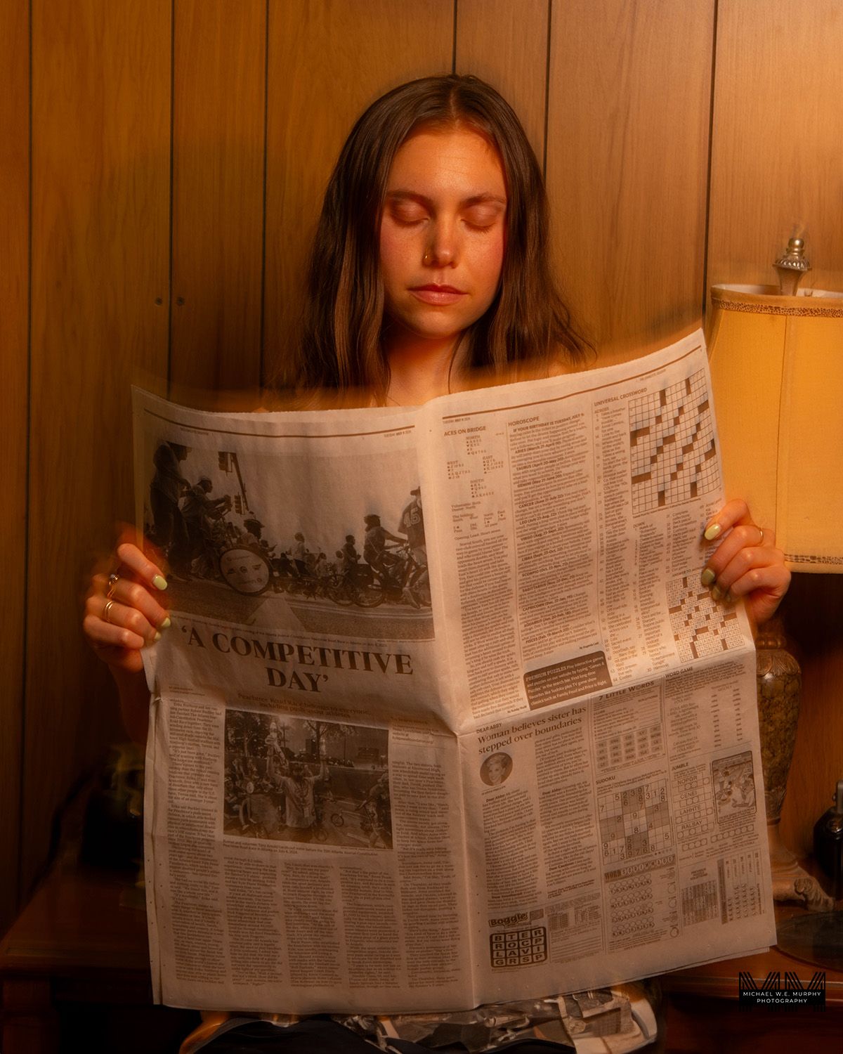 Person reading newspaper section titled 'Competitive Day' in warm ambient light.