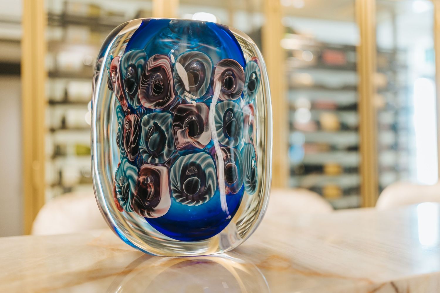 Decorative glass vase with blue swirls and artistic patterns on wooden surface.