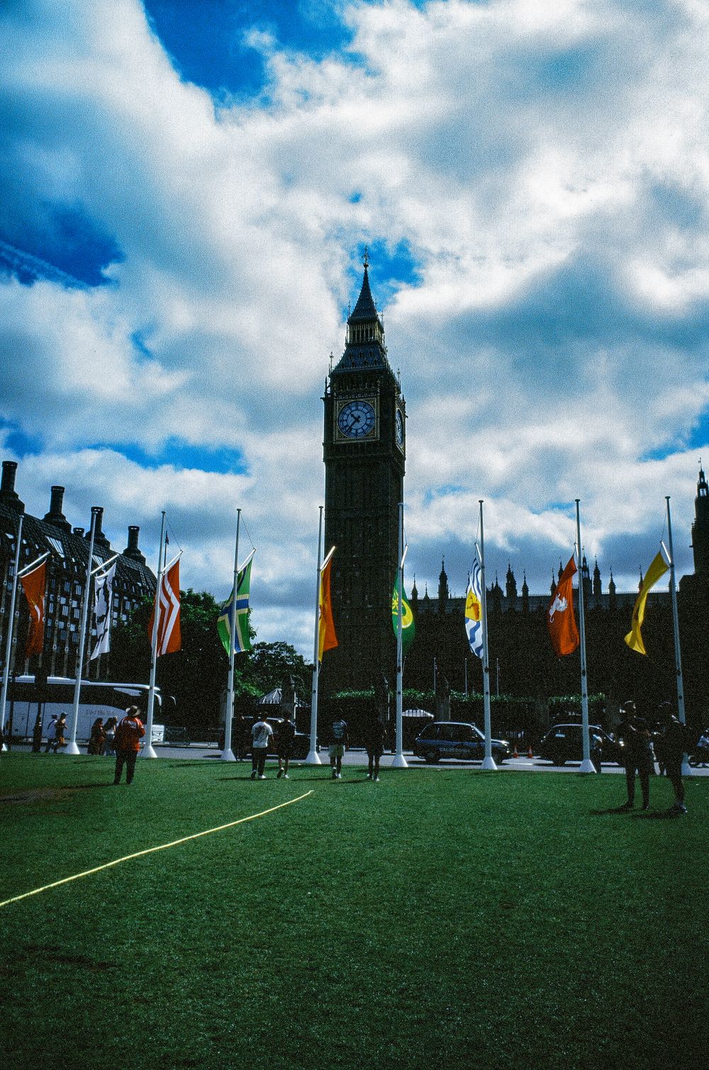 Big Ben tower with international flags and green lawn in Westminster, London.