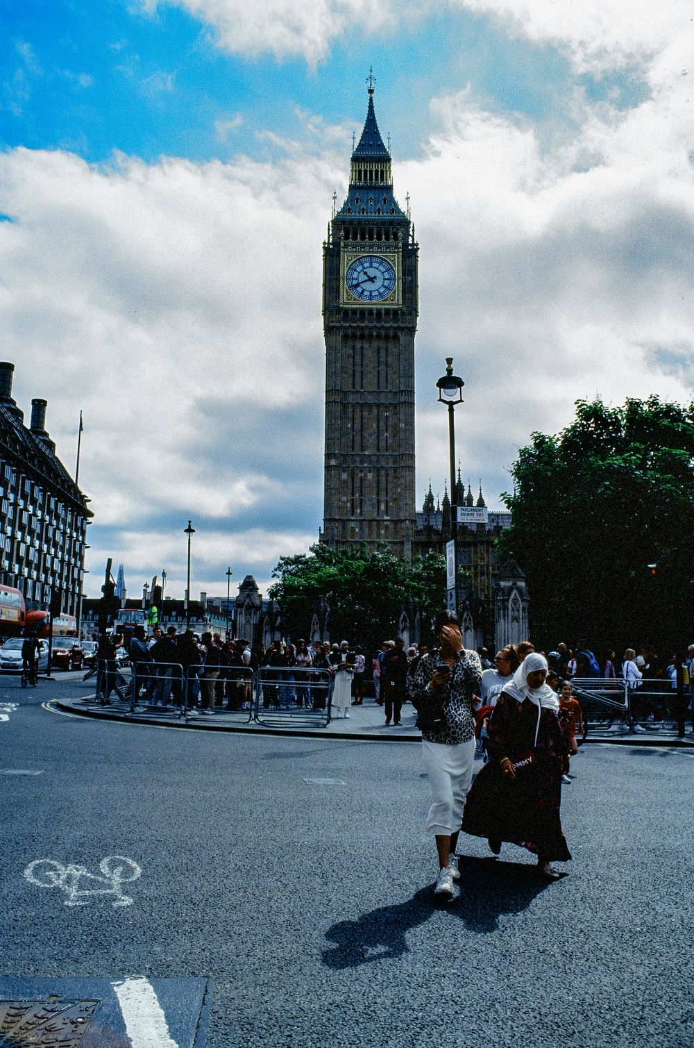 Big Ben tower rising above busy street corner in London with pedestrians walking by.