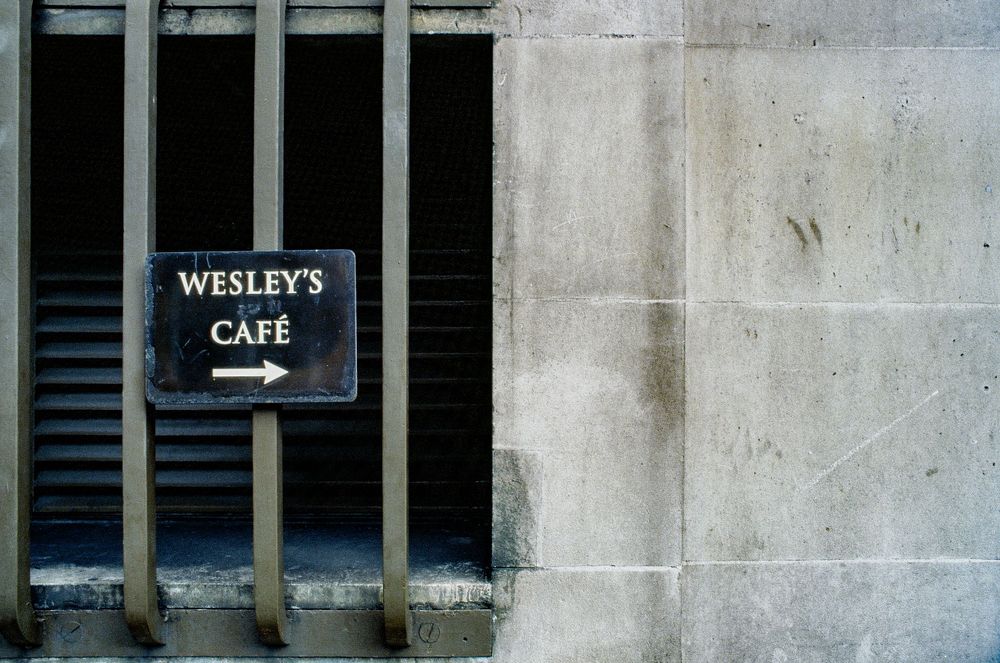 Wesley's Cafe directional sign mounted on stone wall in London.