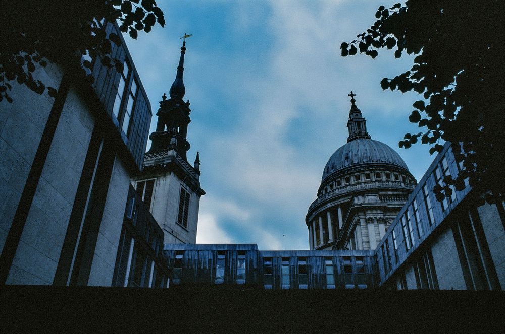 St Paul's Cathedral dome and spire viewed through buildings against blue sky in London.