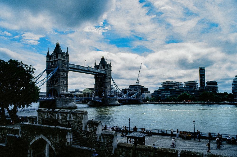 Tower Bridge spans the Thames River under dramatic cloudy London sky.
