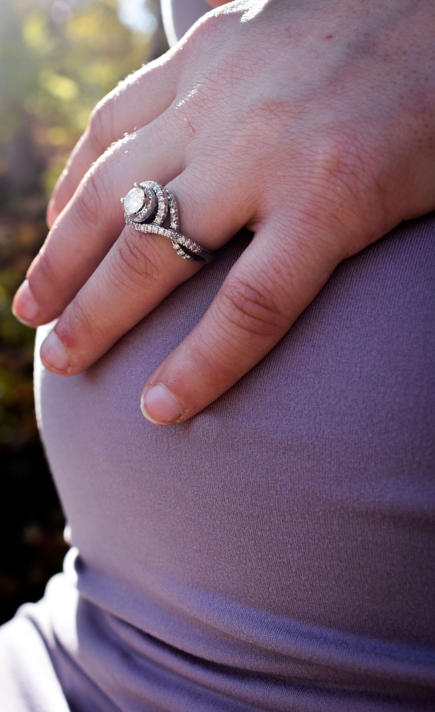 Close-up of ornate engagement ring on hand against purple fabric background.