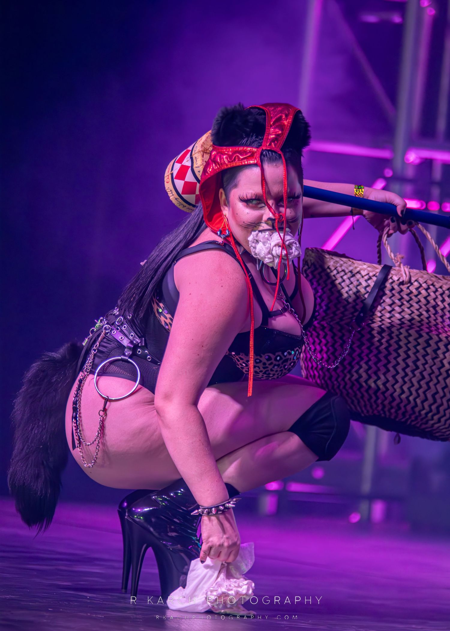 A performer in dark attire crouches on stage under dramatic purple lighting.