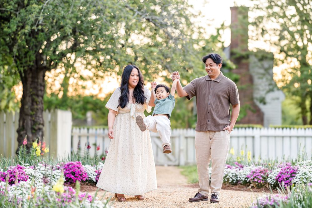 Photography of a mom, dad, and child playing in a garden in Colonial Williamsburg at golden hour in glowy lighting.