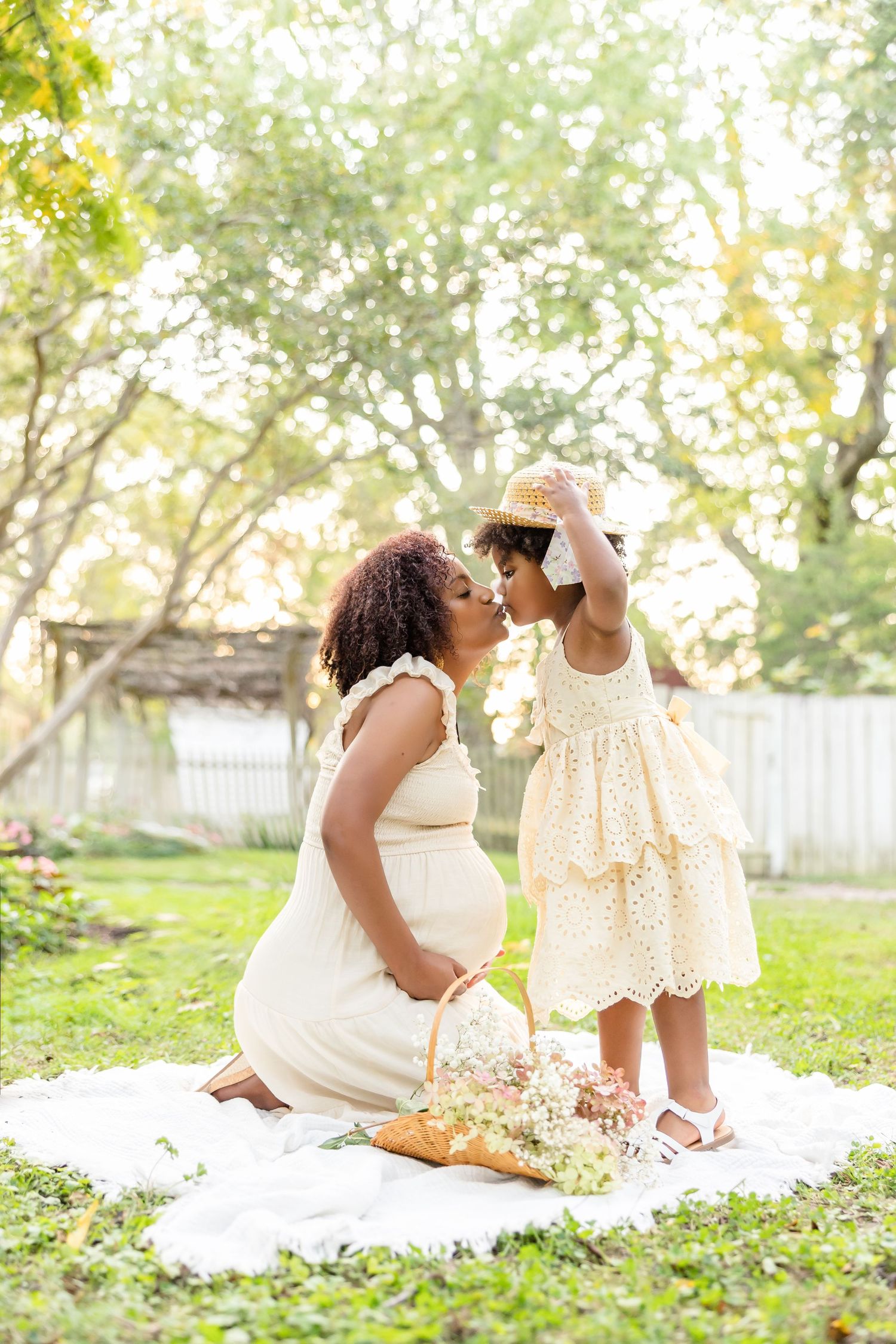 Maternity photography of a mom kissing her daughter while holding her bump. They are posed in a backlit garden in Colonial Williamsburg.