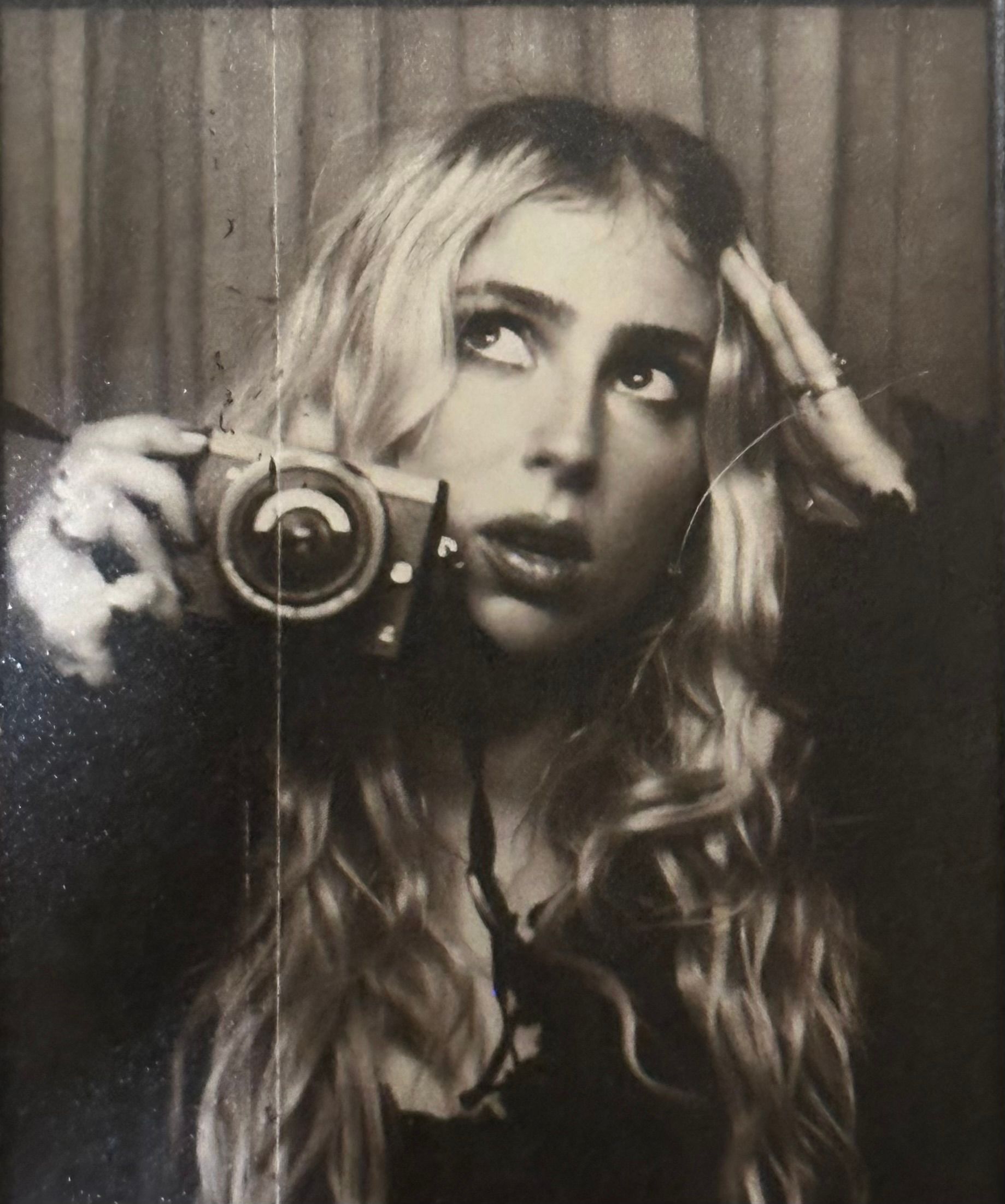 Portrait of someone holding a vintage camera while wearing a denim dress and fuzzy white sweater.