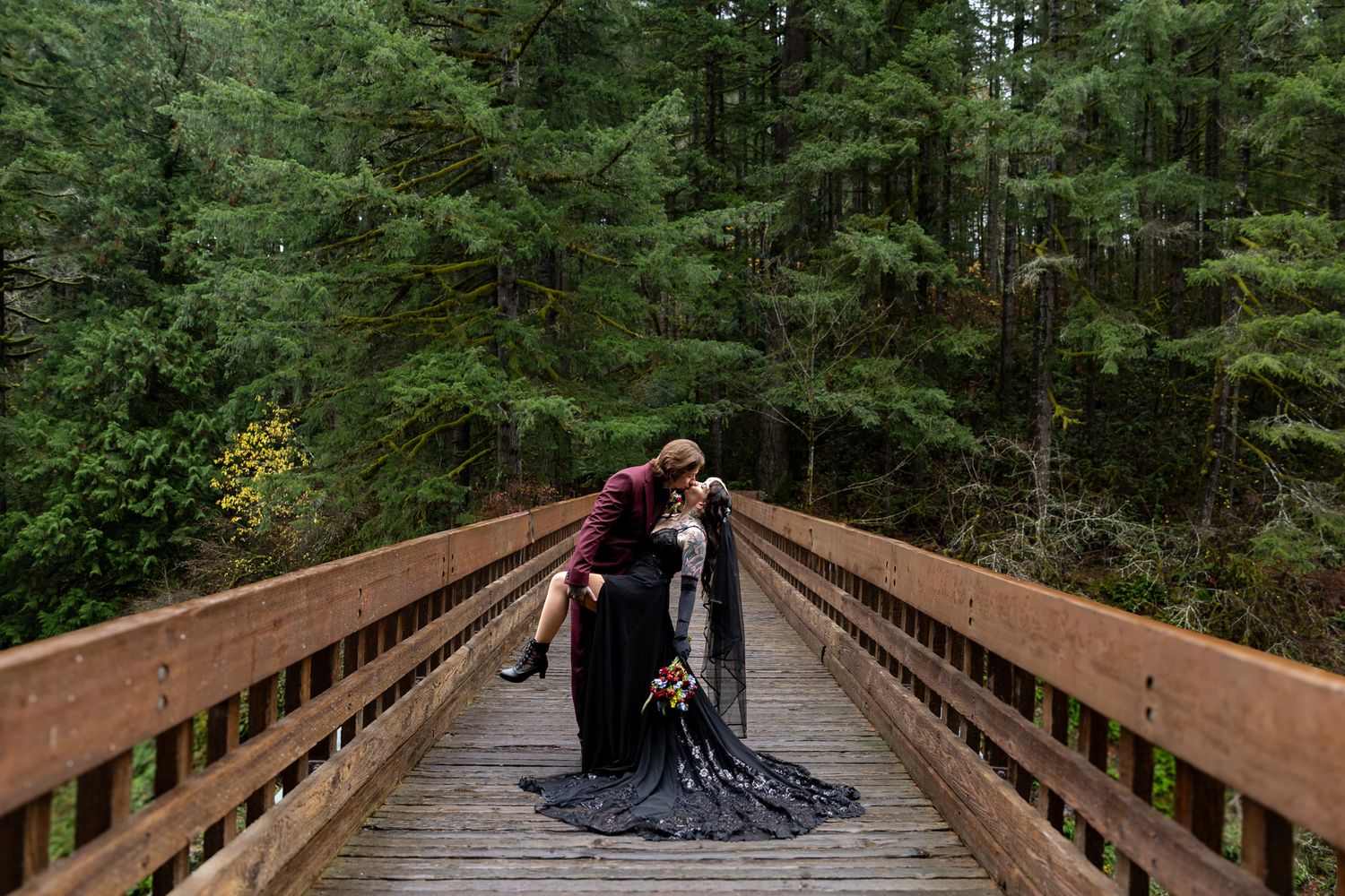 Dark and Moody bride and groom sharing a dip kiss on the bridge at Moulton Falls in Washington State. PNW Elopement Photographer.