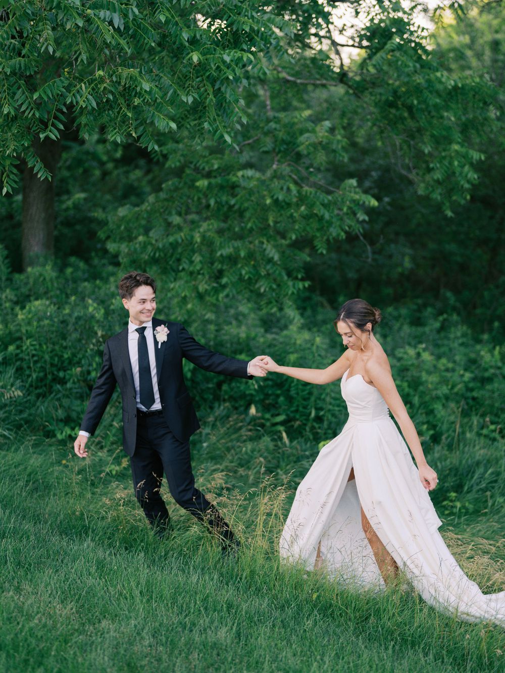 Groom leading Bride walking in a wooded scene at Eloise Mount Horeb. Classic and film-inspired wedding photography in Madison, Wisconsin.