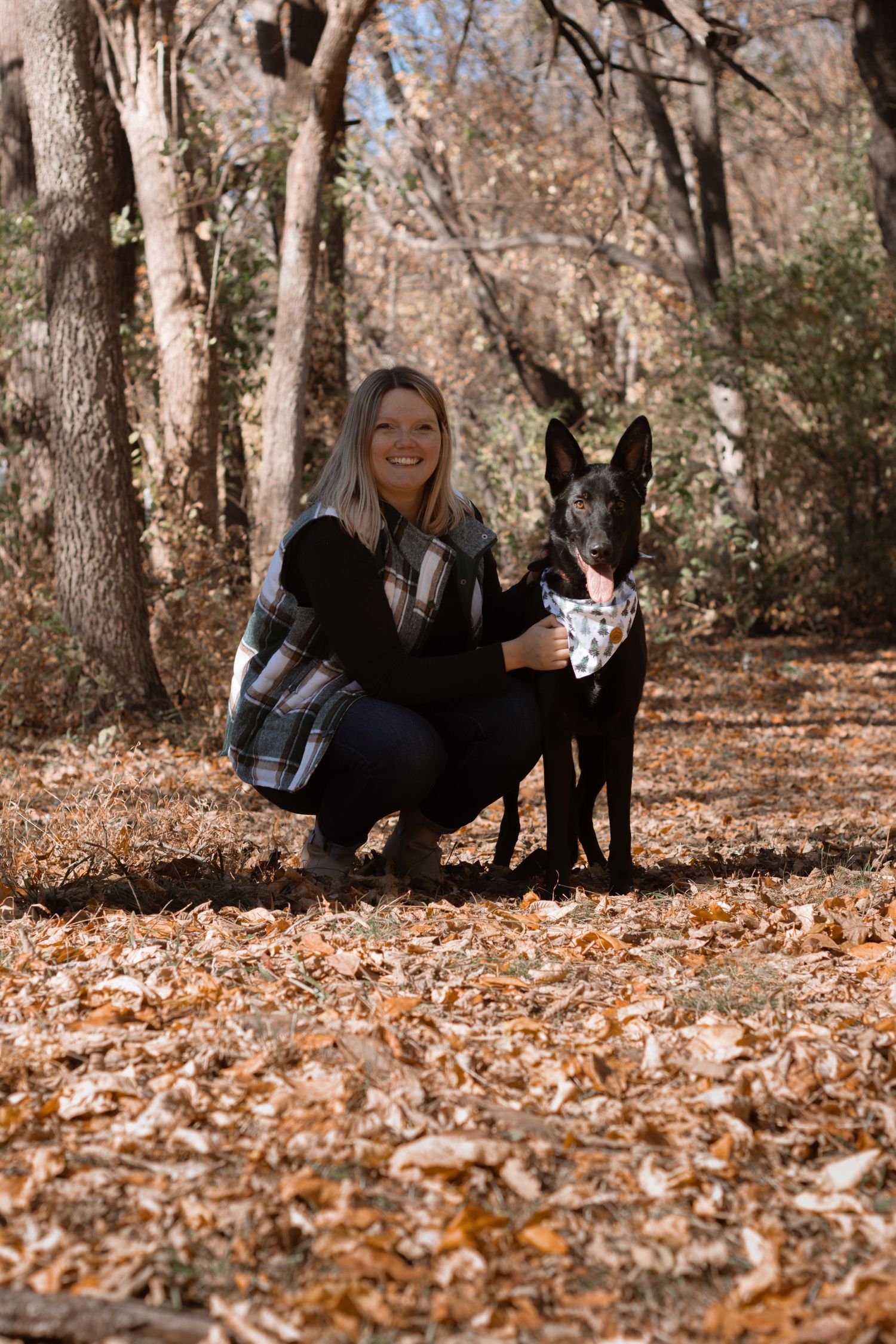 Playful autumn photoshoot with person laying in fallen leaves next to black dog.