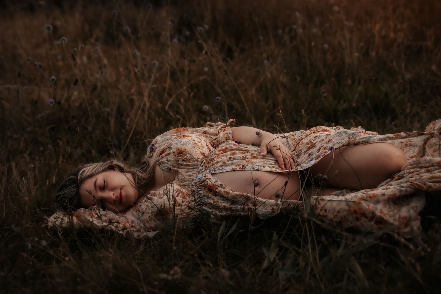 An artistic maternity portrait captures a tender moment at sunset in a mountain setting.