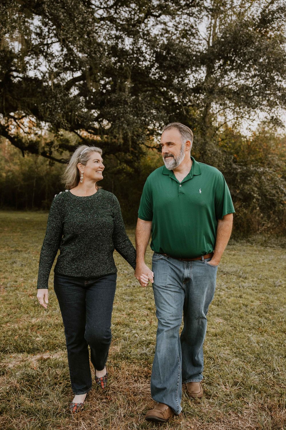 A couple walks hand in hand through a grassy field during golden hour.
