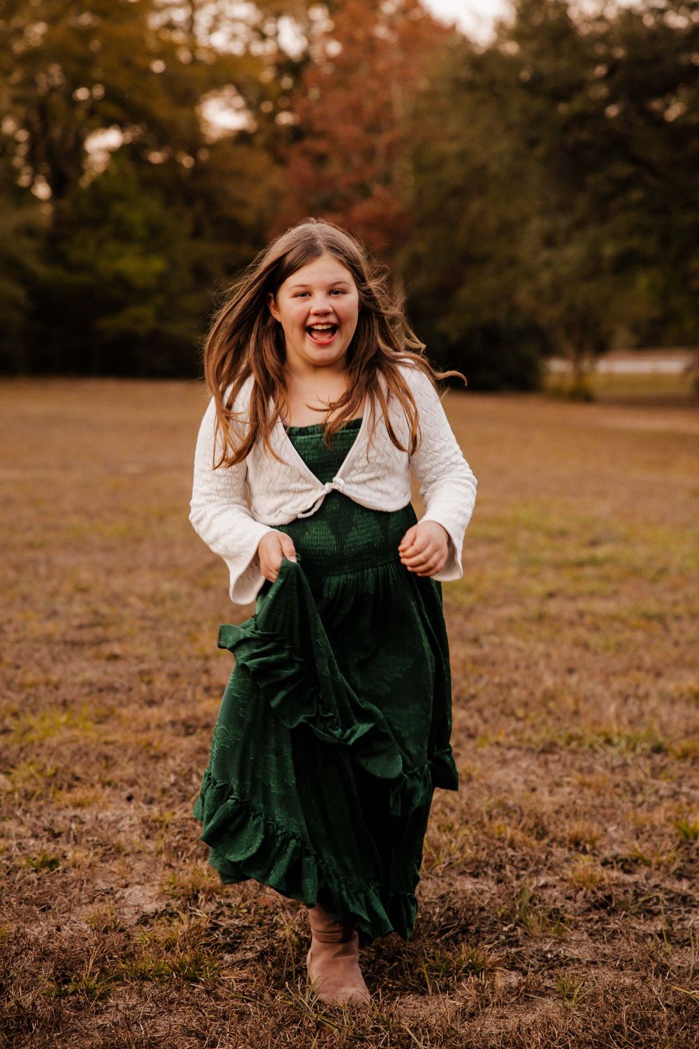 A person in a dark green velvet dress twirls playfully in an autumn field at sunset.