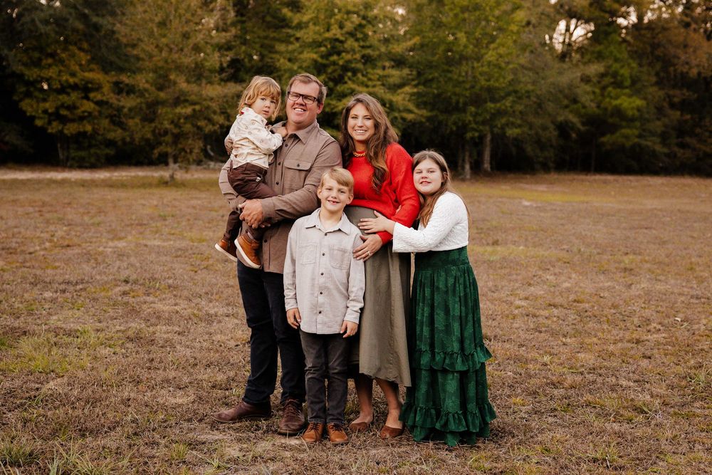 A family group poses together outdoors in coordinated autumn outfits.