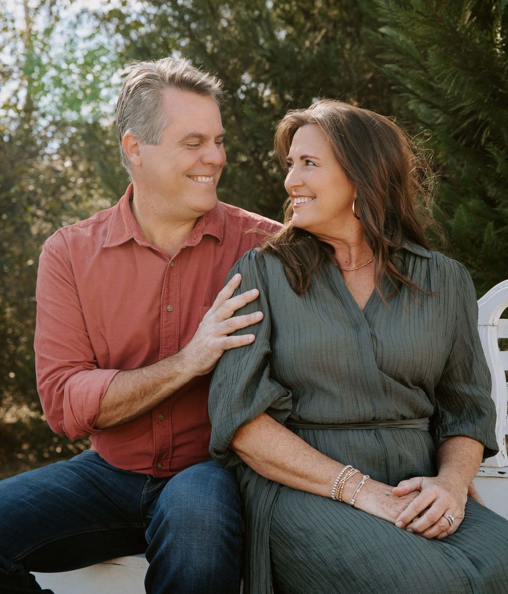 Couple sits close together on white bench sharing intimate moments during outdoor photoshoot.