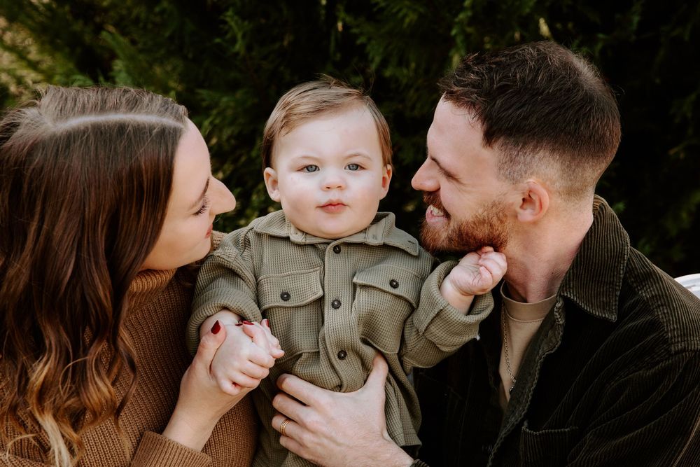 Parents cuddle and smile with their baby during casual outdoor family photo session.