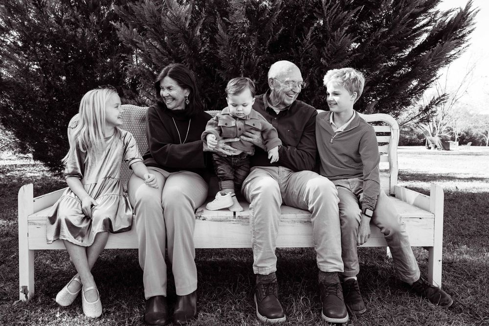 Black and white portrait of family members sitting together on white benches outdoors.