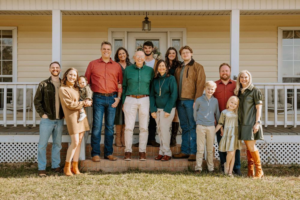 Large family group portrait taken outside a white farmhouse with a porch.