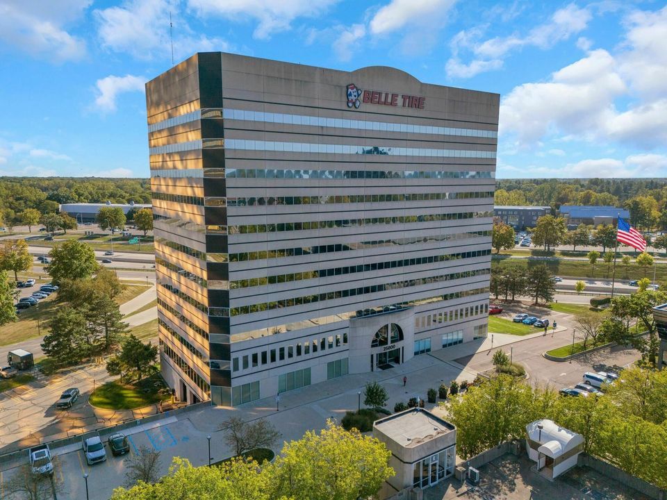Tall multi-story office building with reflective glass facade and Belle Tire signage under a blue sky.