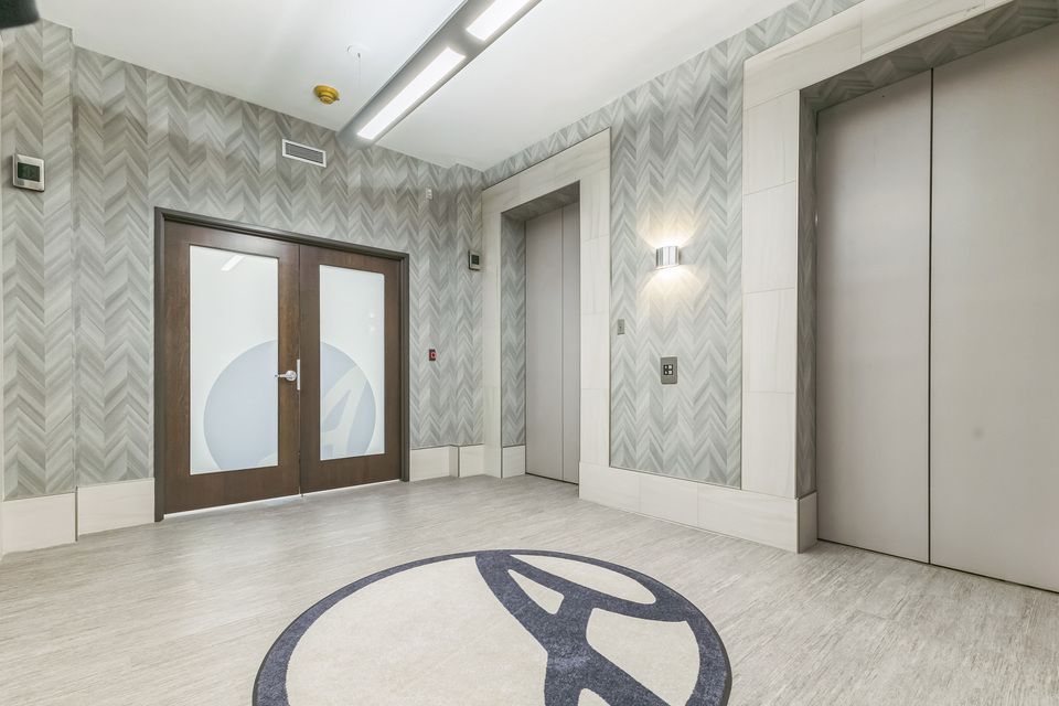 Modern building lobby with herringbone tile walls, decorative floor medallion, and double glass doors.