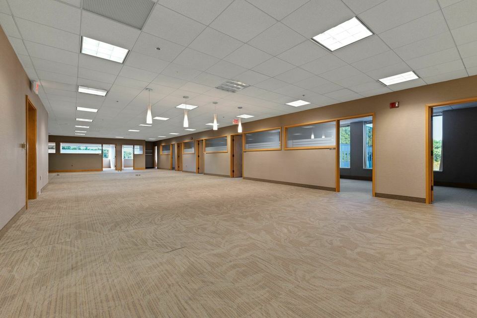 Large empty office space with beige carpet, pendant lights, and private office rooms.
