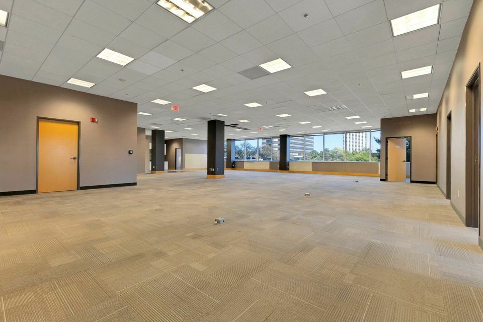 Spacious open-plan office space with neutral carpet and large windows offering city views.