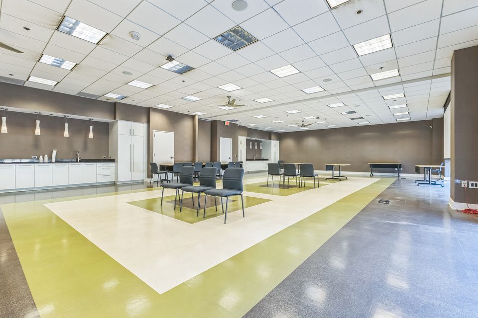 Bright open office breakroom with yellow-green floors, gray chairs, and pendant lights.
