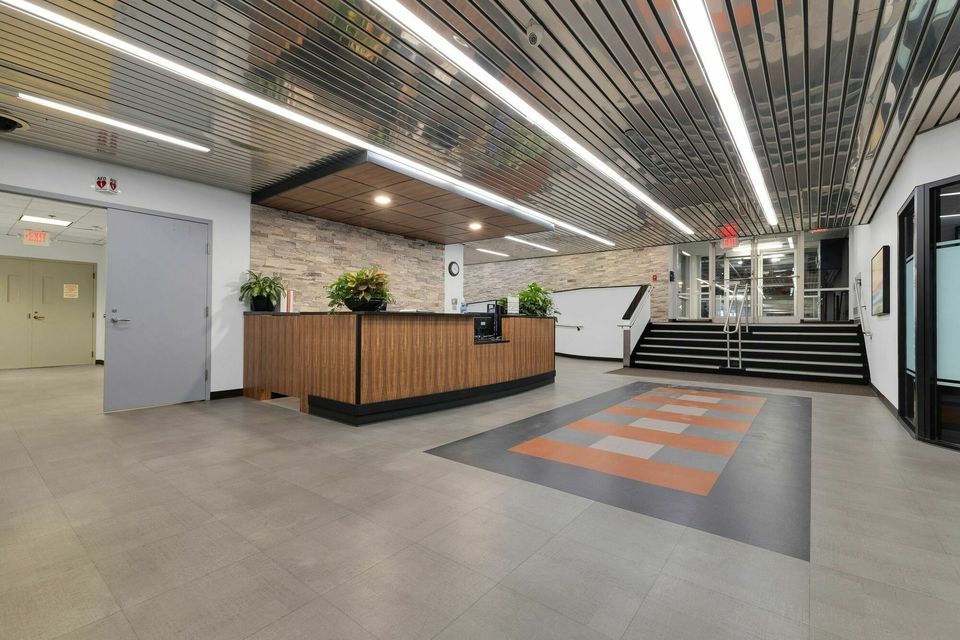 Modern building lobby with wood reception desk, brick accents, and grand staircase.
