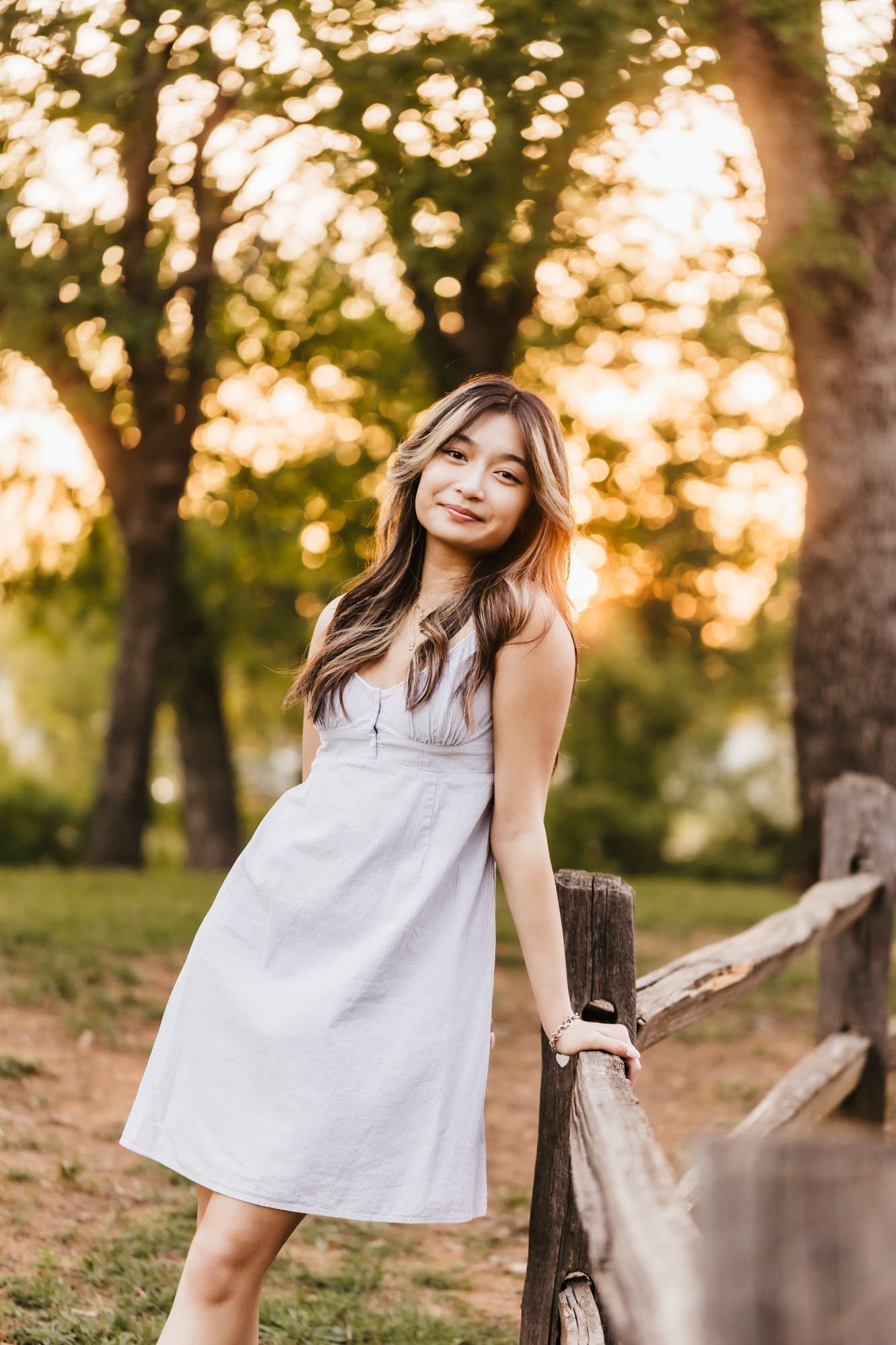 Woman in white dress poses by wooden fence during golden hour.