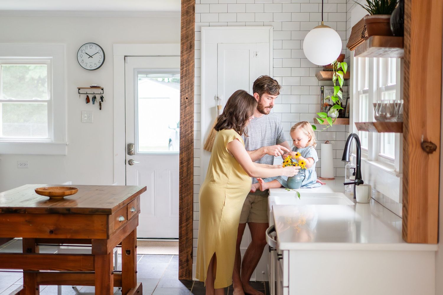 Family washing dishes together in modern white kitchen with wooden accents.