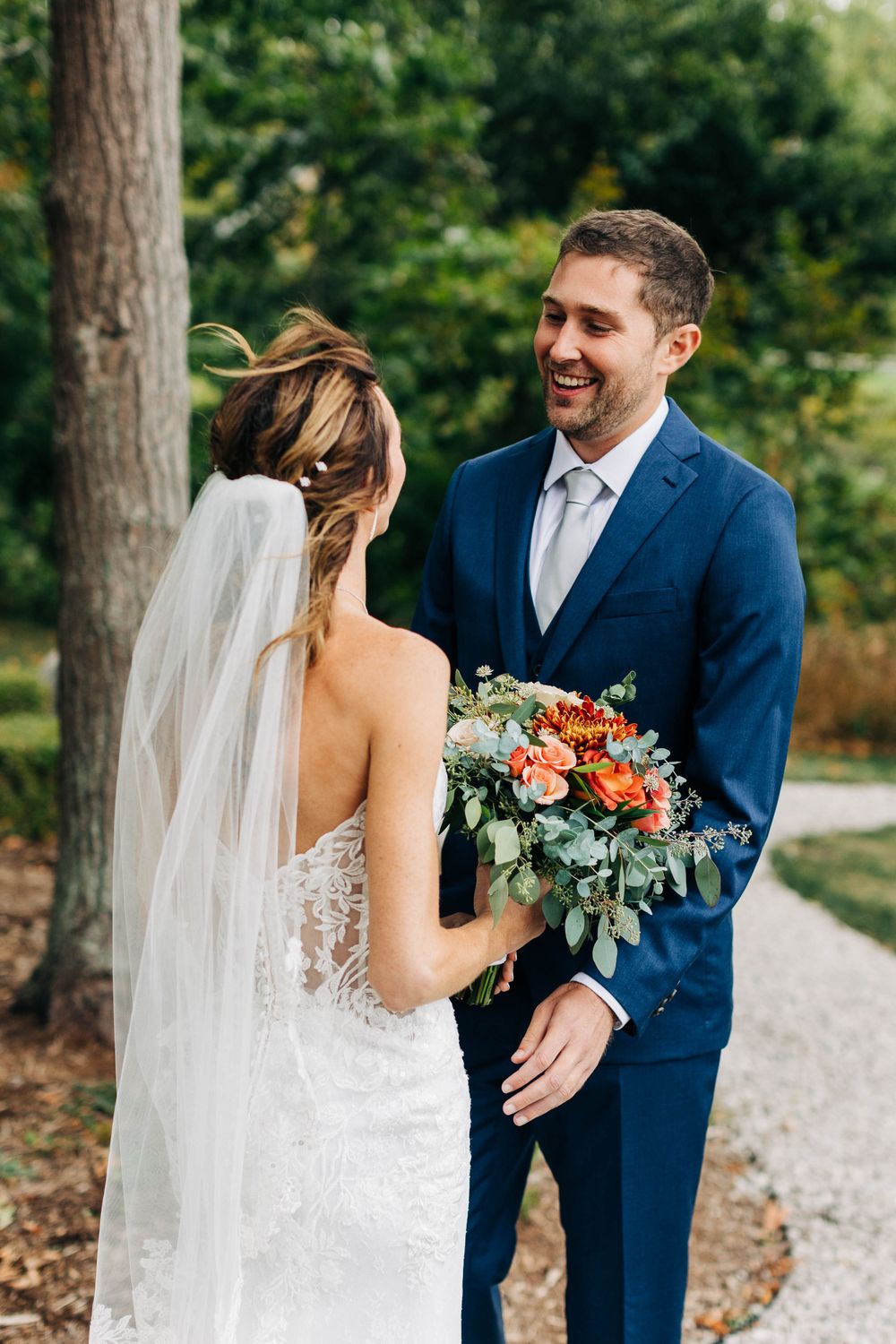 Newlyweds share a joyful moment on garden path with vibrant orange and pink wedding bouquet.