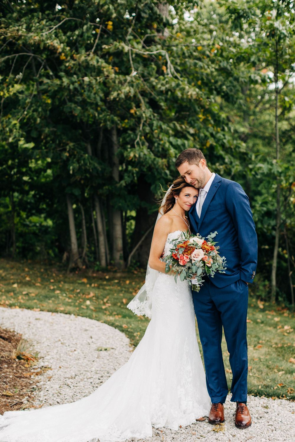 Romantic wedding portrait on gravel path with bride holding coral and blush bouquet.