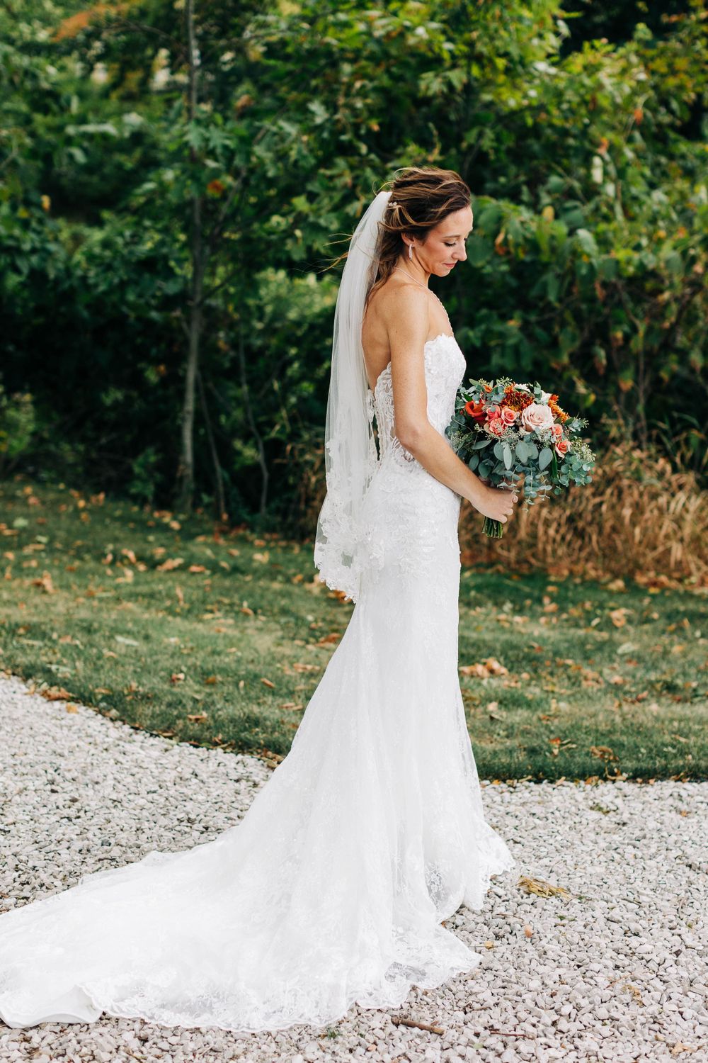 Side view of bride in fitted lace gown with flowing train on garden path.