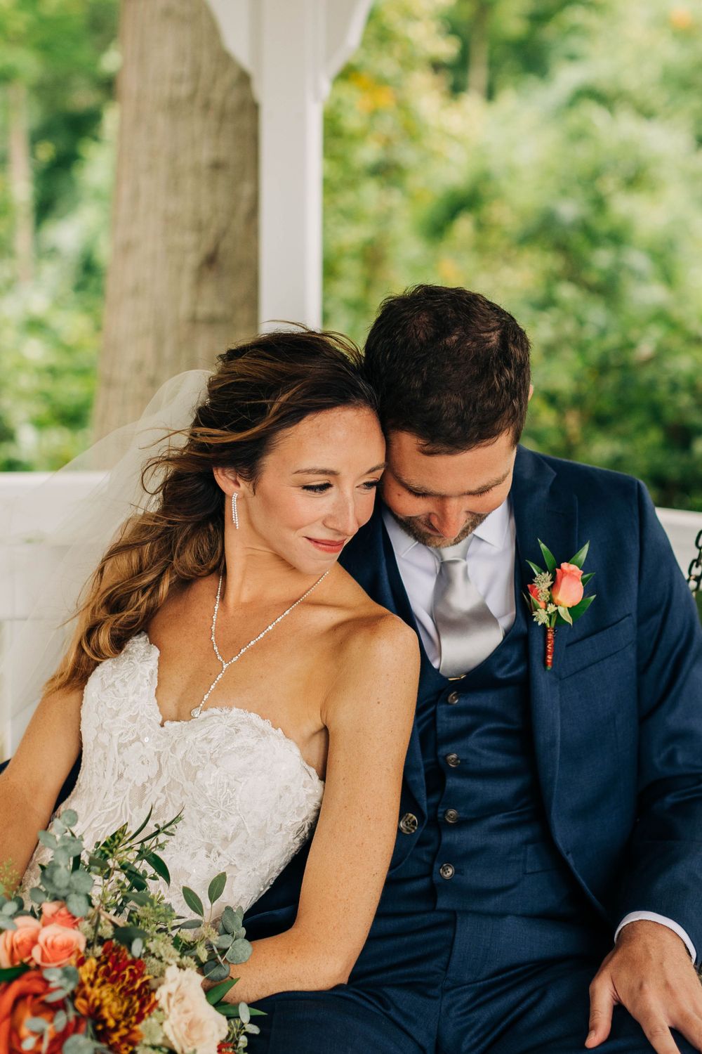 Intimate moment between newlyweds sitting in white gazebo with colorful floral bouquet.